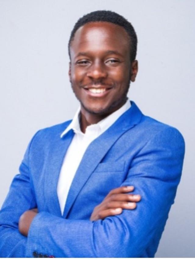 Portrait of a man in a blue blazer and white shirt, arms crossed, studio background.