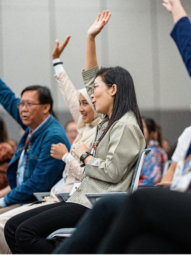 Diverse audience in a conference room raises hands during a session.