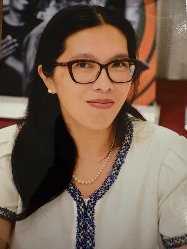 Photograph of a woman with dark hair and glasses, wearing a white blouse with blue embroidery.