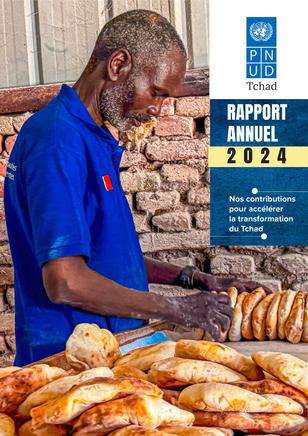 Man in a blue shirt preparing bread with a brick wall in the background.