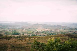 Vast landscape view with rolling hills, greenery, and a cloudy sky.