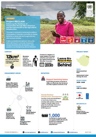 A man in a pink shirt smiles while holding a mobile phone in a lush, green field.