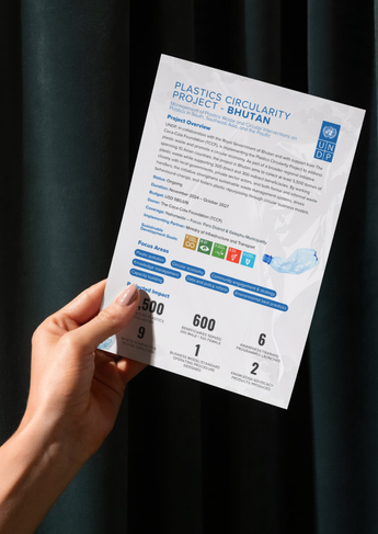 A person holding a brochure or paper against a dark curtain background.