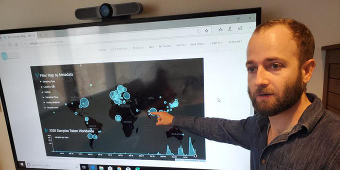 A man gestures toward a digital map displaying global data on a screen.