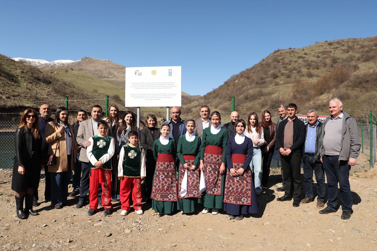 Group of people posing outdoors in a desert valley with a banner in the background.