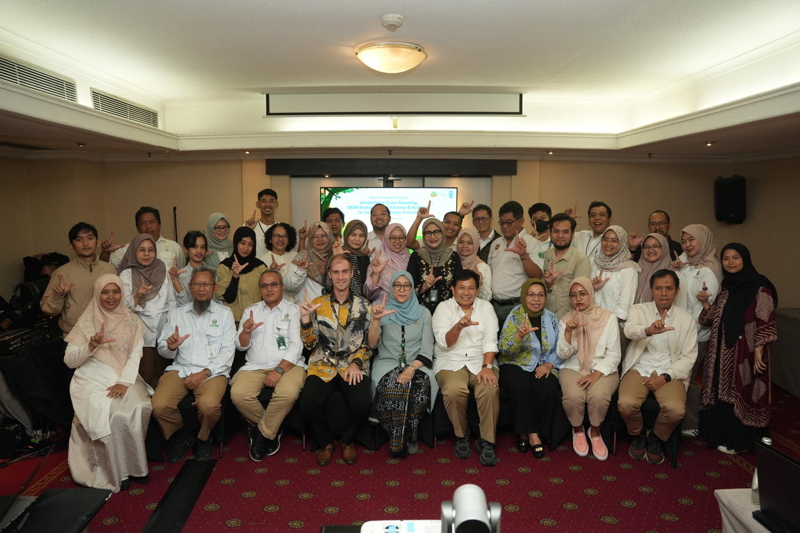 Large group of people in white attire posing for a group photo in a conference room.