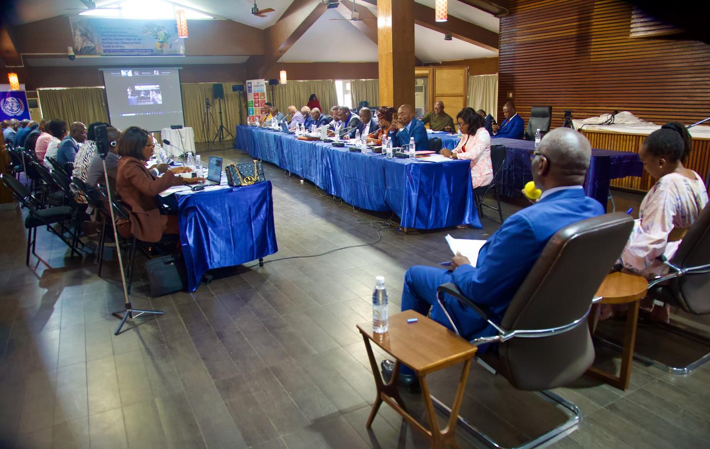 People seated around a U-shaped conference table with blue cloths in a wood-paneled room.