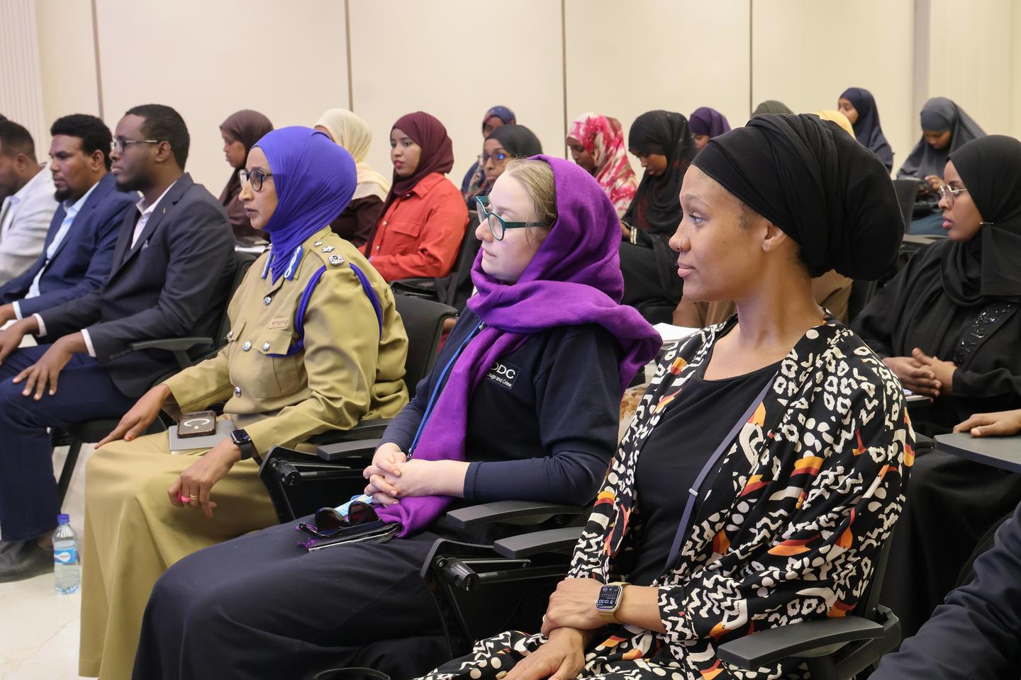 Audience seated in a conference hall; many women wearing colorful hijabs.