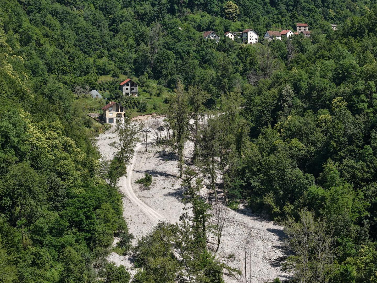 Aerial view of a winding light-gray road through a dense forest hillside.