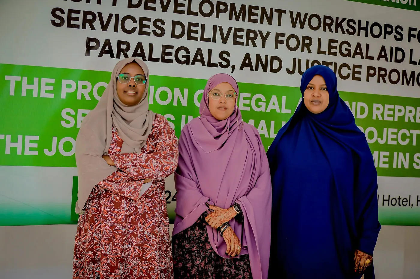 Three women in hijabs pose and smile in front of a green event banner.