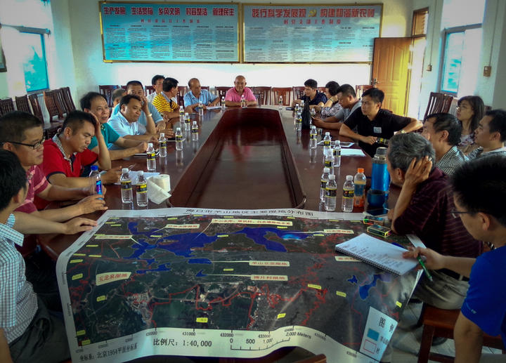 A group meeting around a large table with a detailed map, discussing plans.