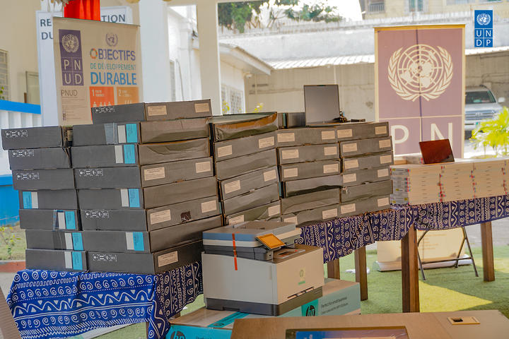 Stacks of long gray boxes on pallets in a donation center, with blue crates nearby.